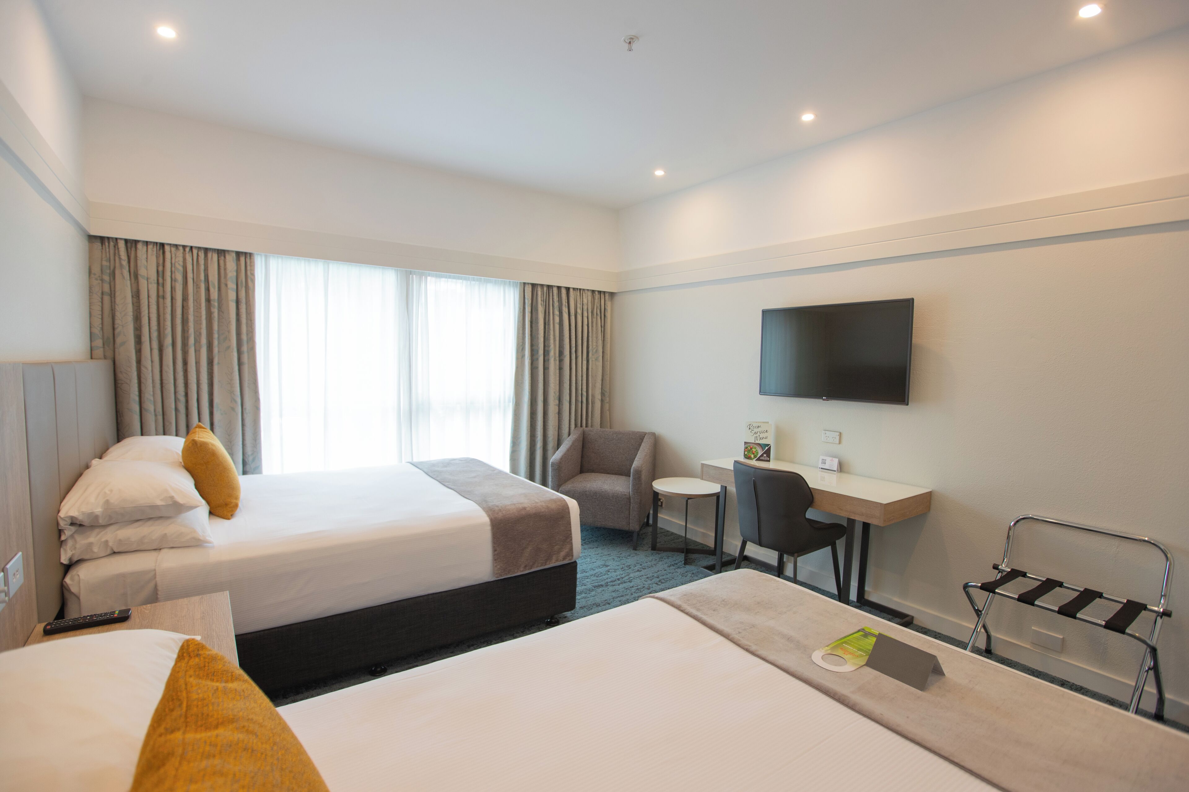 A hotel room with two beds, a desk, a chair, a TV, and a small table.
