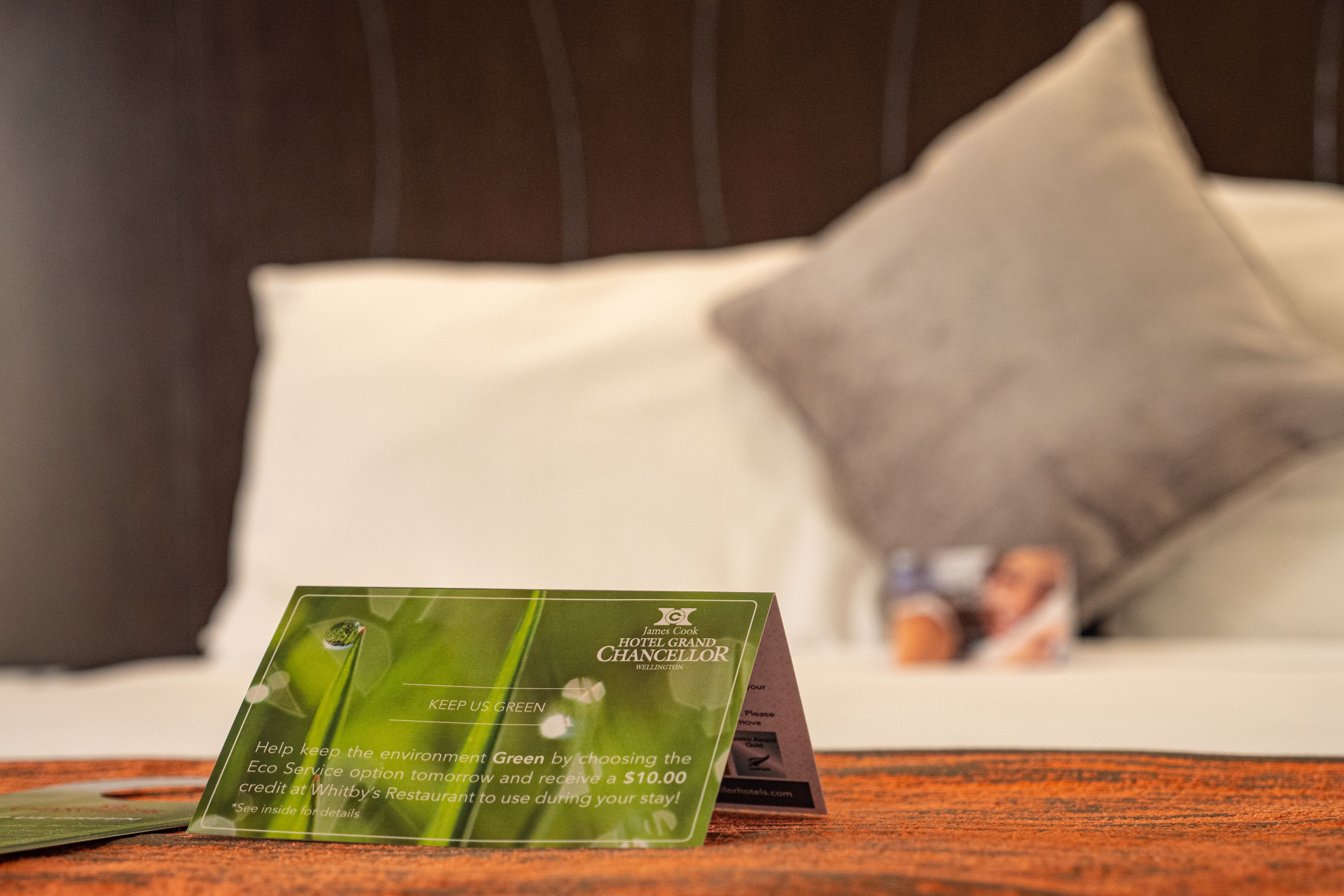 Una tarjeta de información del hotel verde sobre una cama con un almohadón y un fondo desenfocado.