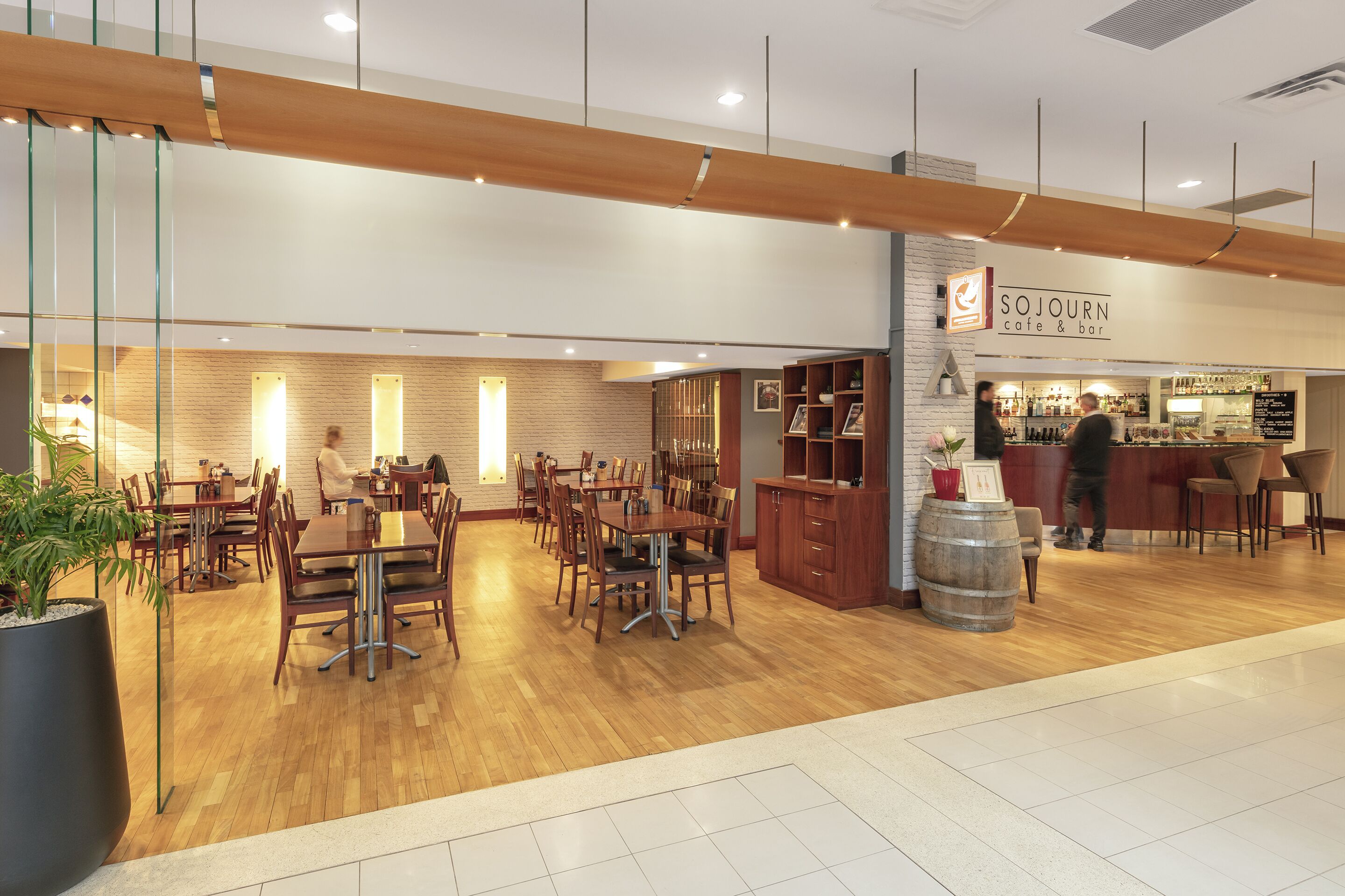 A modern cafe with wooden tables and chairs, a bar area, and a visible menu board.