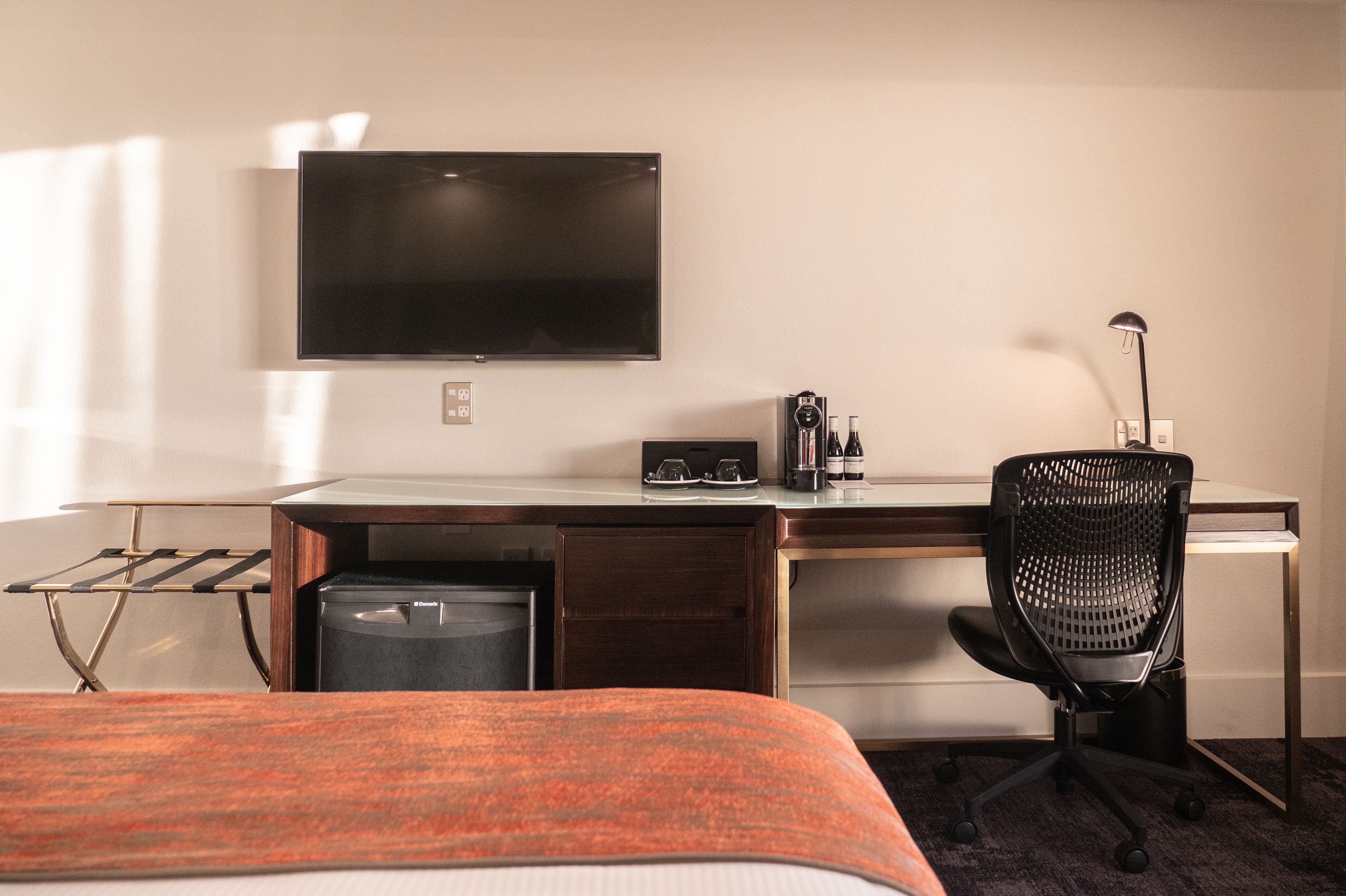 A hotel room with a bed, a desk with a computer, a chair, a TV, and a coffee maker.