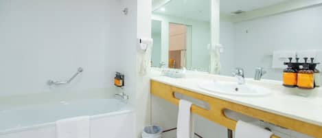 A modern bathroom with a bathtub, two sinks, a large mirror, and a trash bin.