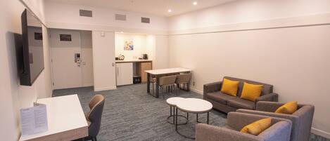 A hotel room with a dining area, a sofa, a small table, and a TV mounted on the wall.