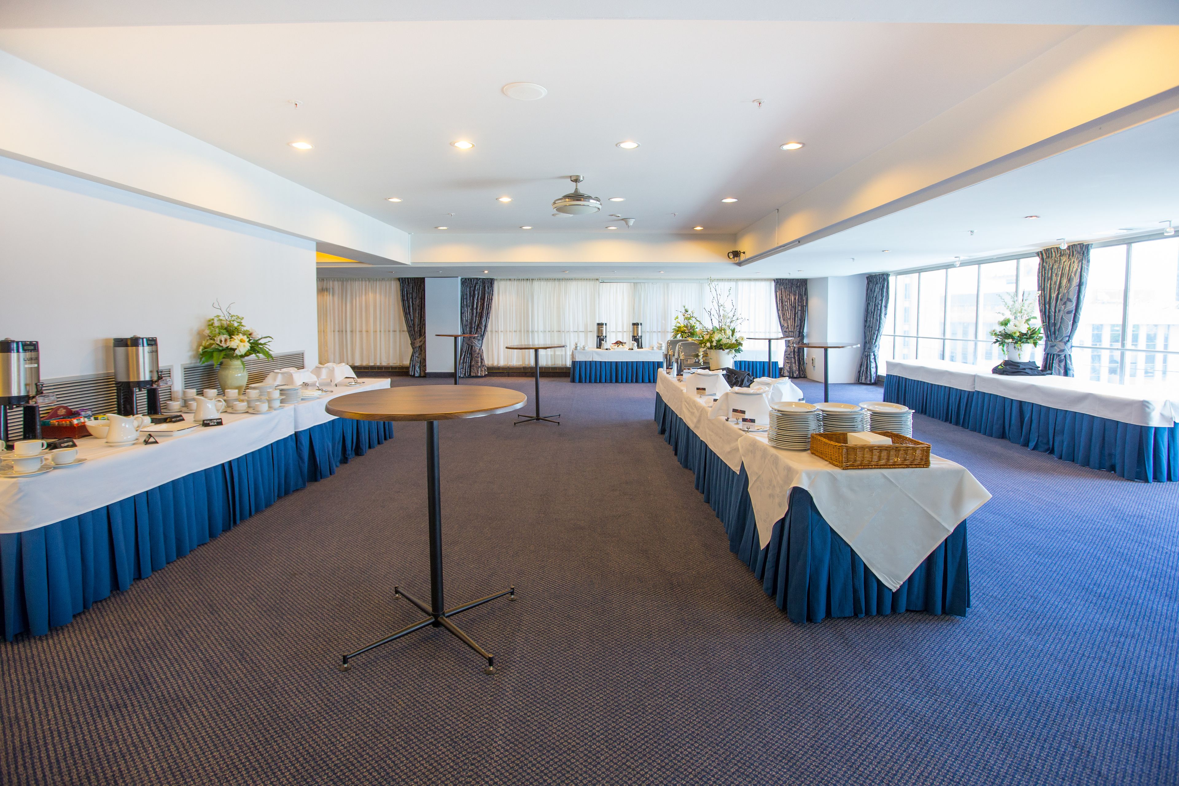 Un salón de conferencias con mesas largas, manteles blancos y cortinas azules.