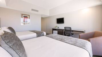 Habitación de hotel con dos camas, un escritorio, una silla, un televisor y una ventana con cortinas.