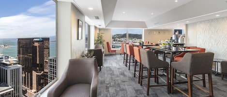 A modern hotel room with a city view, a bar area, and a dining space.