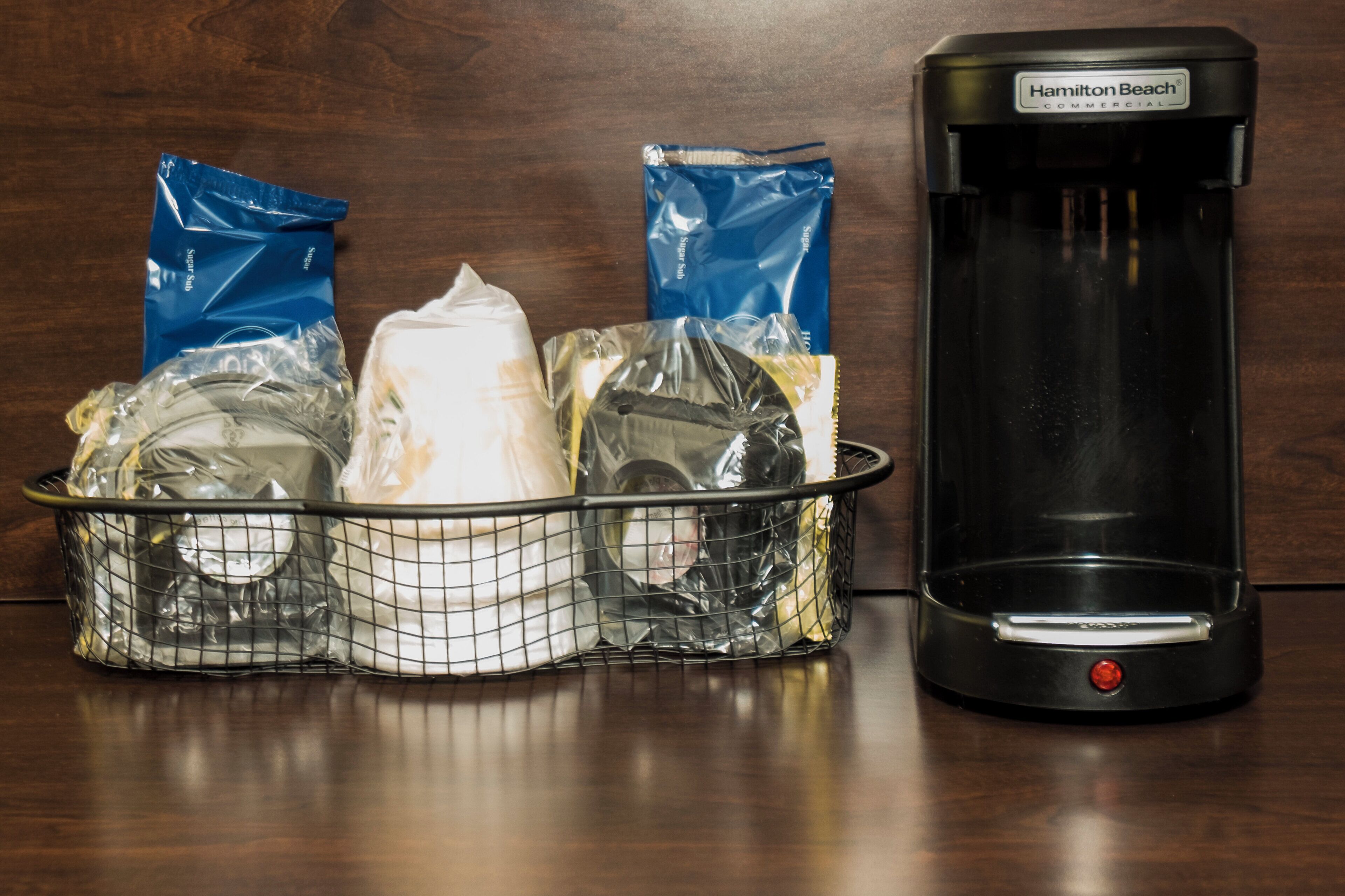 A coffee maker and a basket of food items on a wooden surface.