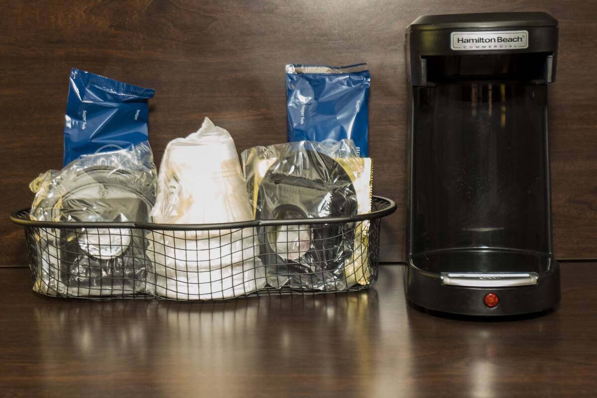 Uma cafeteira e uma cesta com diversos objetos sobre uma superfície de madeira.