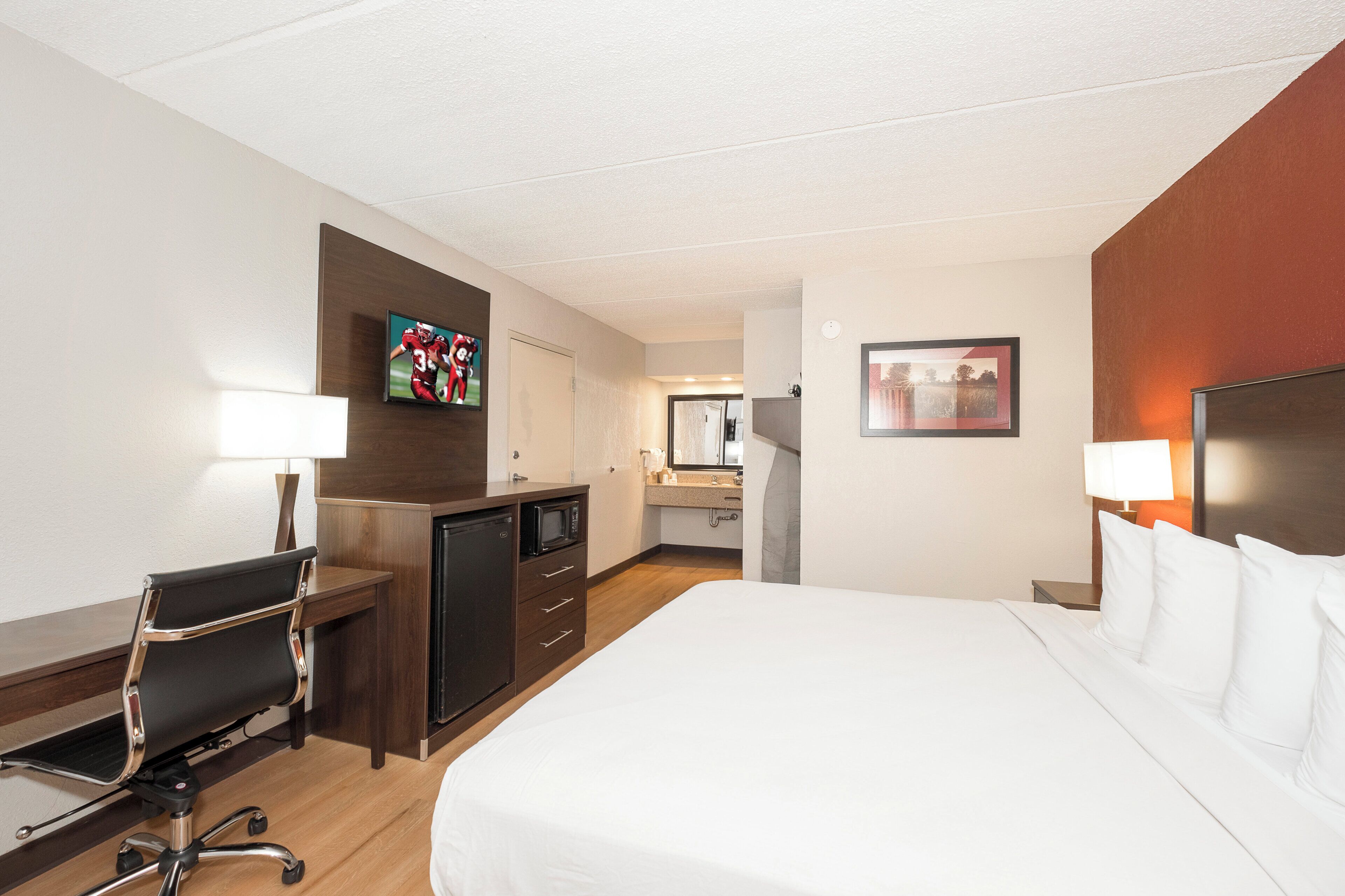 Ein Hotelzimmer mit Bett, Schreibtisch, Stuhl, Fernseher und einem sichtbaren Badezimmer im Hintergrund.
