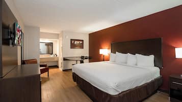 A hotel room with a bed, bedside tables, a desk, a chair, a mirror, and a wall-mounted TV.