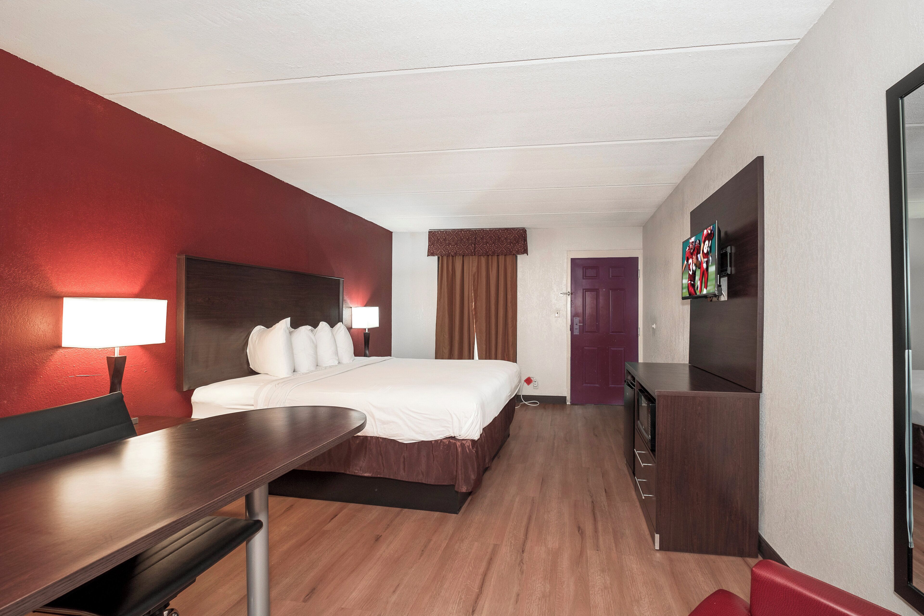Een hotelkamer met een bed, nachtkastje, lamp, televisie en een deur.