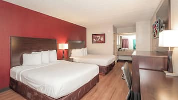 Quarto de hotel com duas camas, uma escrivaninha, uma cadeira, um abajur e um quadro na parede.