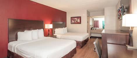 A hotel room with two beds, a desk, a chair, a lamp, and a framed picture on the wall.