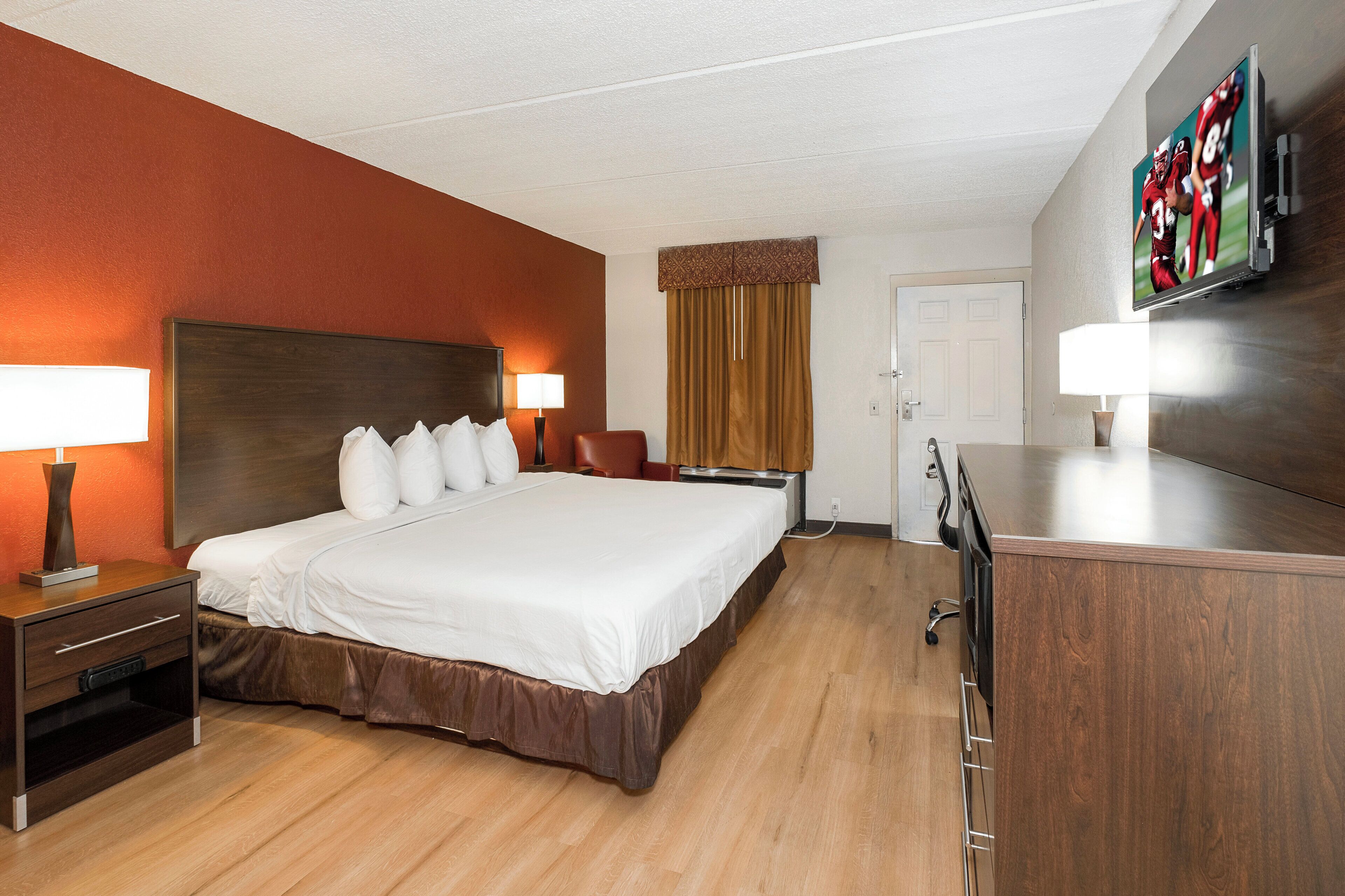 A hotel room with a large bed, bedside lamps, a desk with a chair, a television, and a door.
