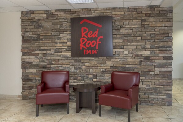 Placa do Red Roof Inn numa parede de tijolos, duas poltronas de couro e uma pequena mesa redonda.