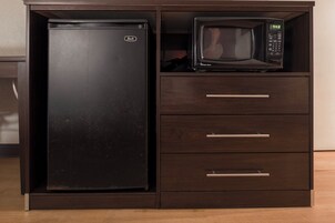 A black refrigerator and a microwave placed inside a wooden cabinet with three drawers.
