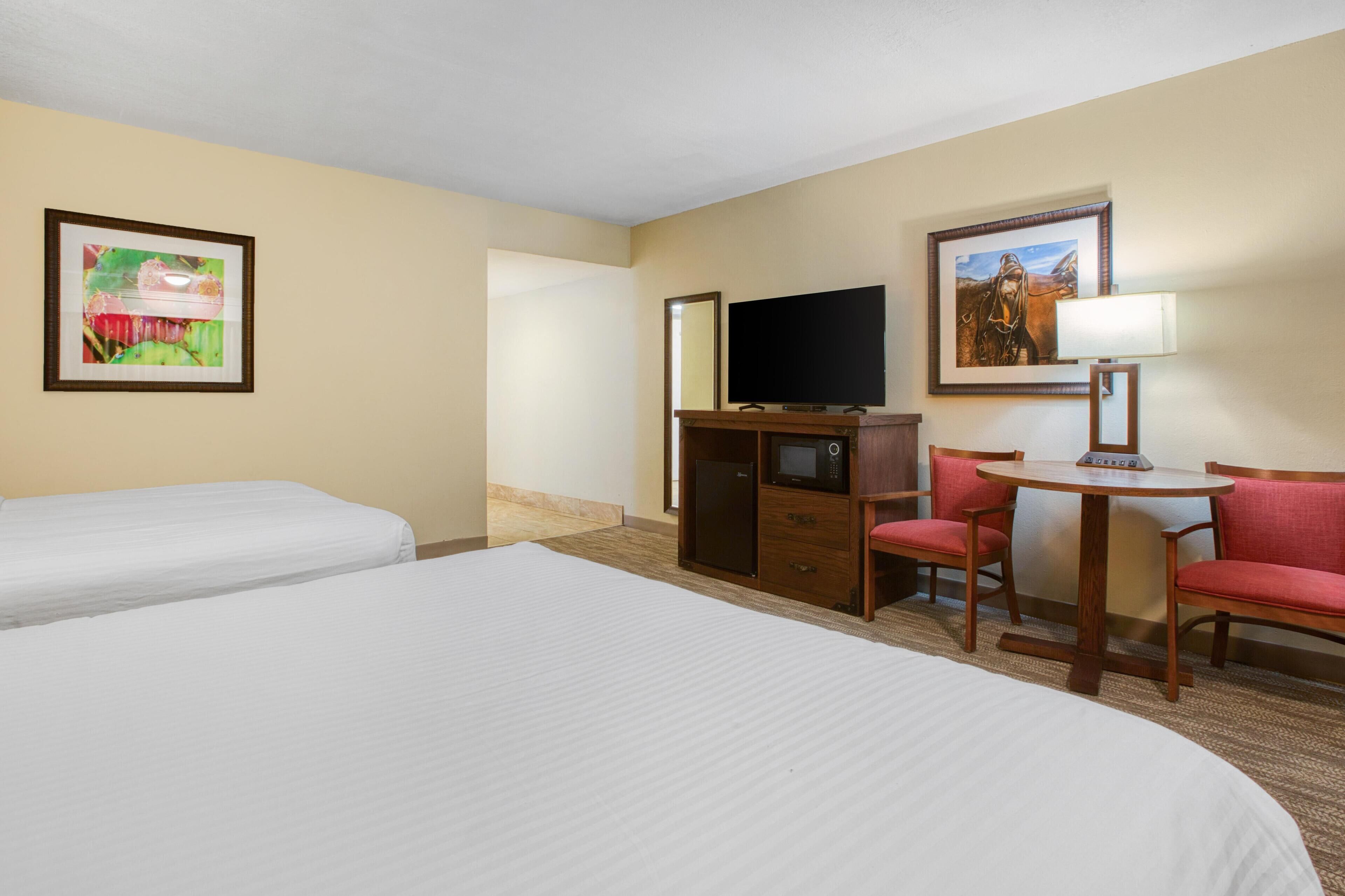 A hotel room with two beds, a desk with a computer, a TV, and two chairs.