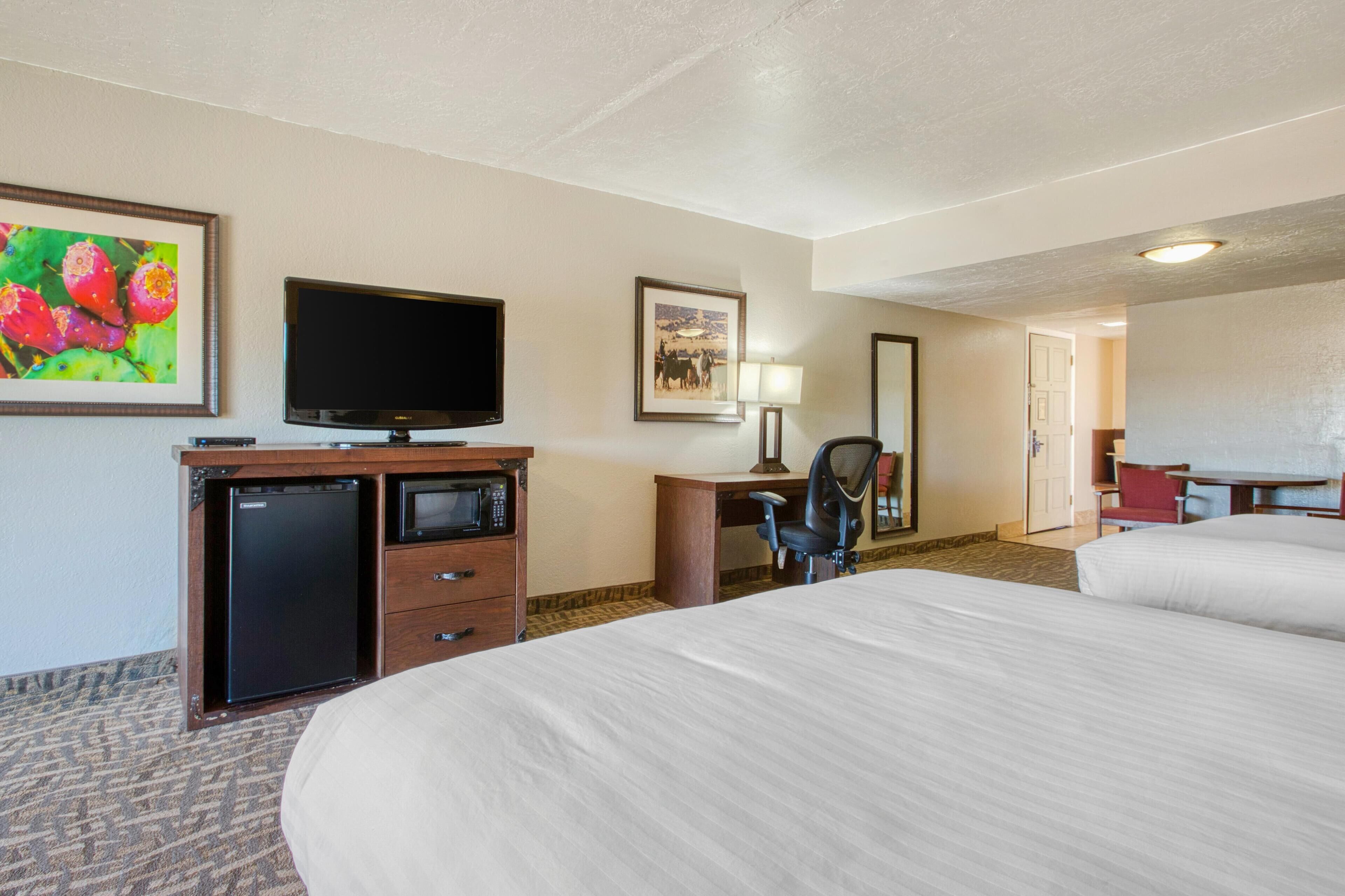Una camera d'albergo con un letto, una scrivania con computer, televisione, forno a microonde e frigorifero.