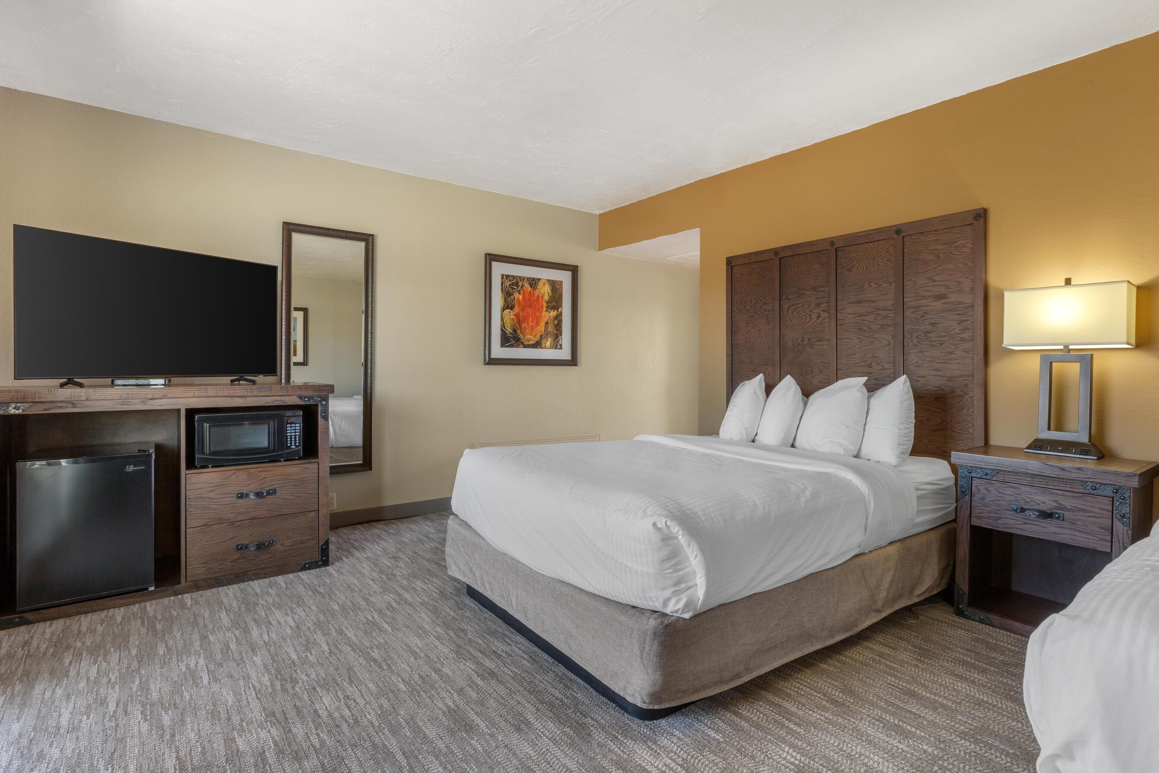 A hotel room with a bed, a desk with a television and microwave, and a nightstand with a lamp.