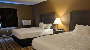 A hotel room with two beds, a bedside table with a lamp, a clock, and a window with curtains. - Magnuson Hotel Copper Crown (Hancock)
