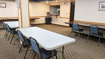 A conference room with a long table, several chairs, a trash can, and an exit sign.