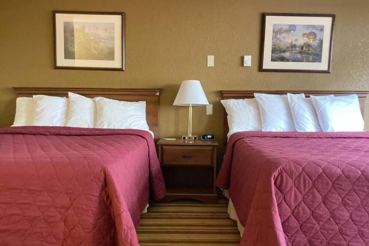 A hotel room with two beds, a nightstand with a lamp, and framed pictures on the wall.