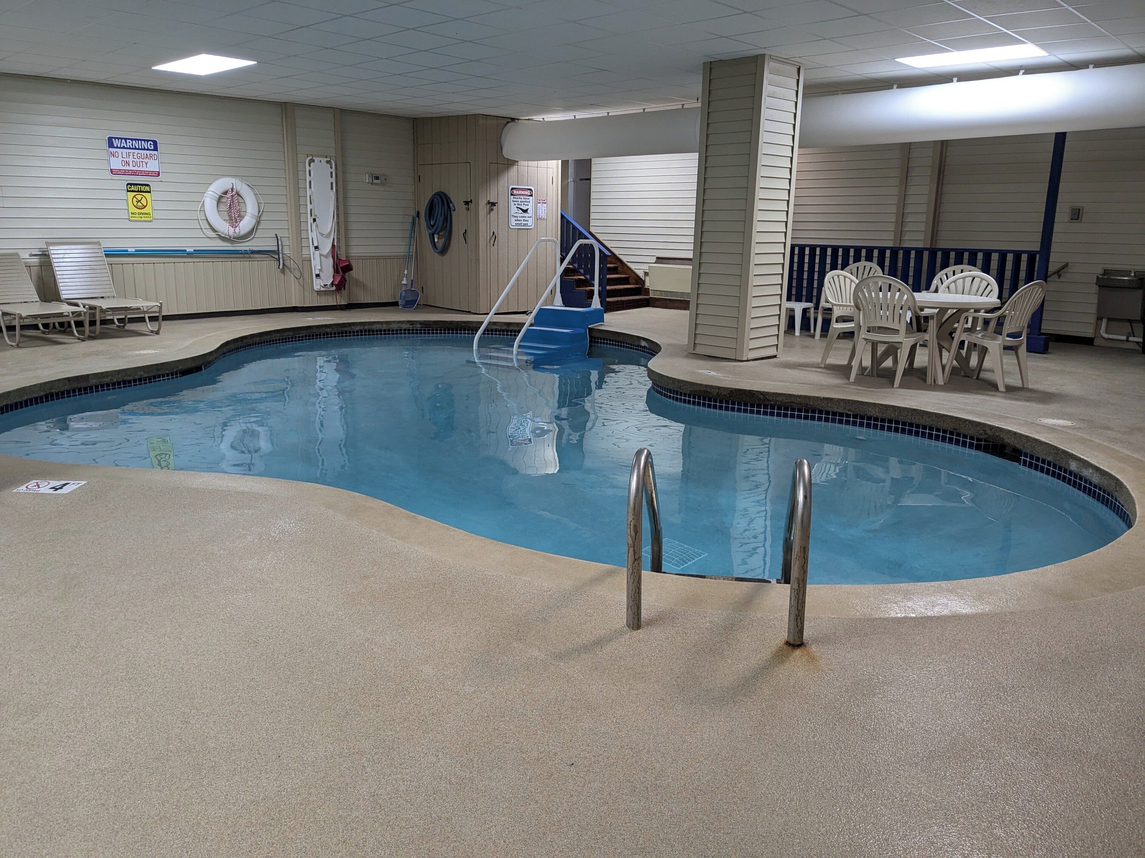 An indoor swimming pool with a lifeguard chair, lounge chairs, and a staircase leading to a deck area.