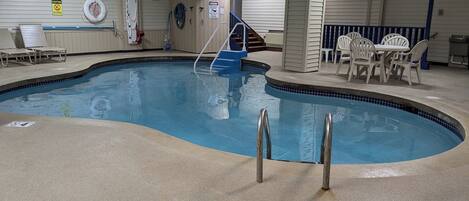 An indoor swimming pool with a lifeguard chair, lounge chairs, and a staircase leading to a deck area.