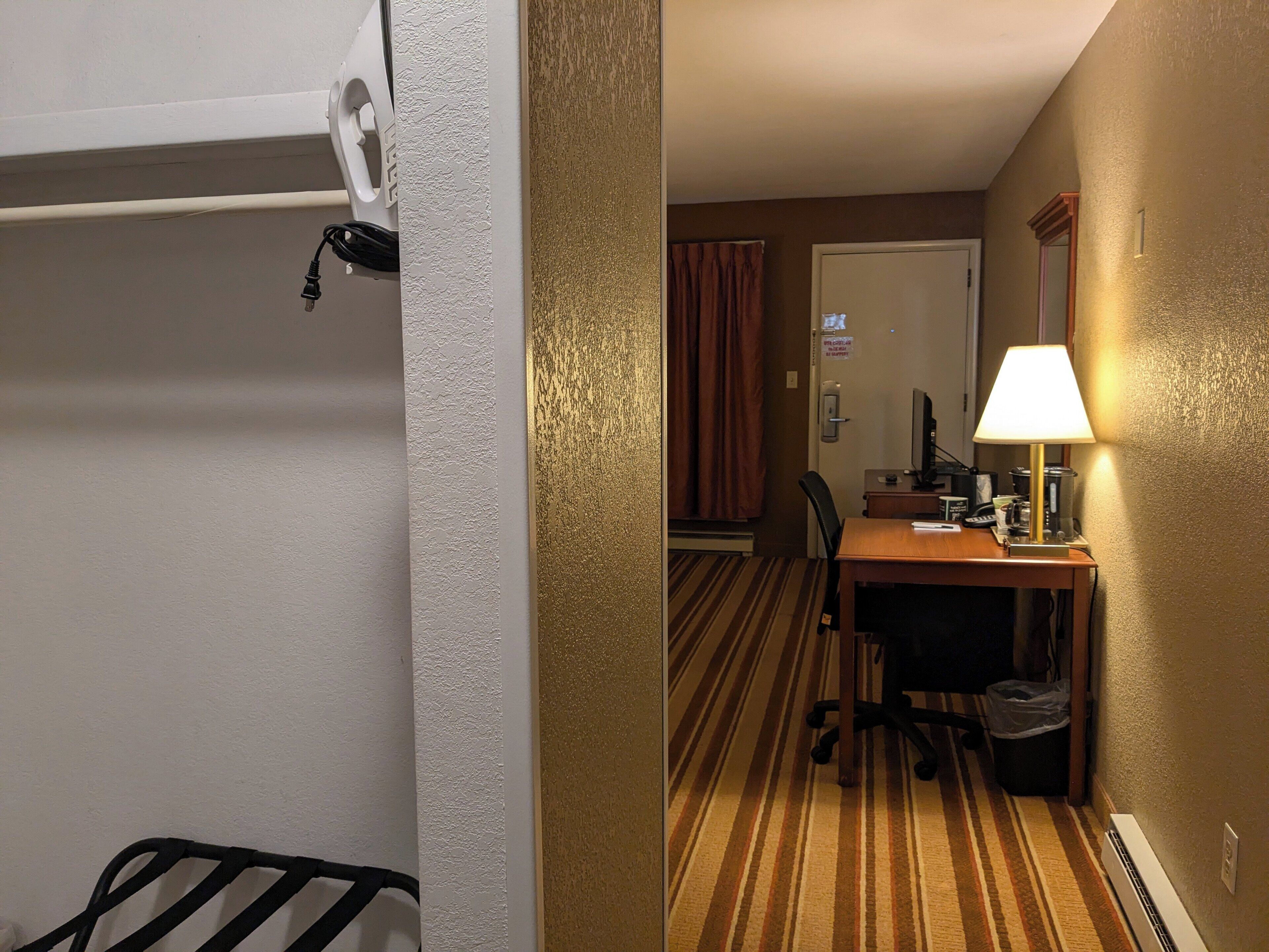Een hotelkamer met een bed, een bureau met een computer, een lamp en een stoel.