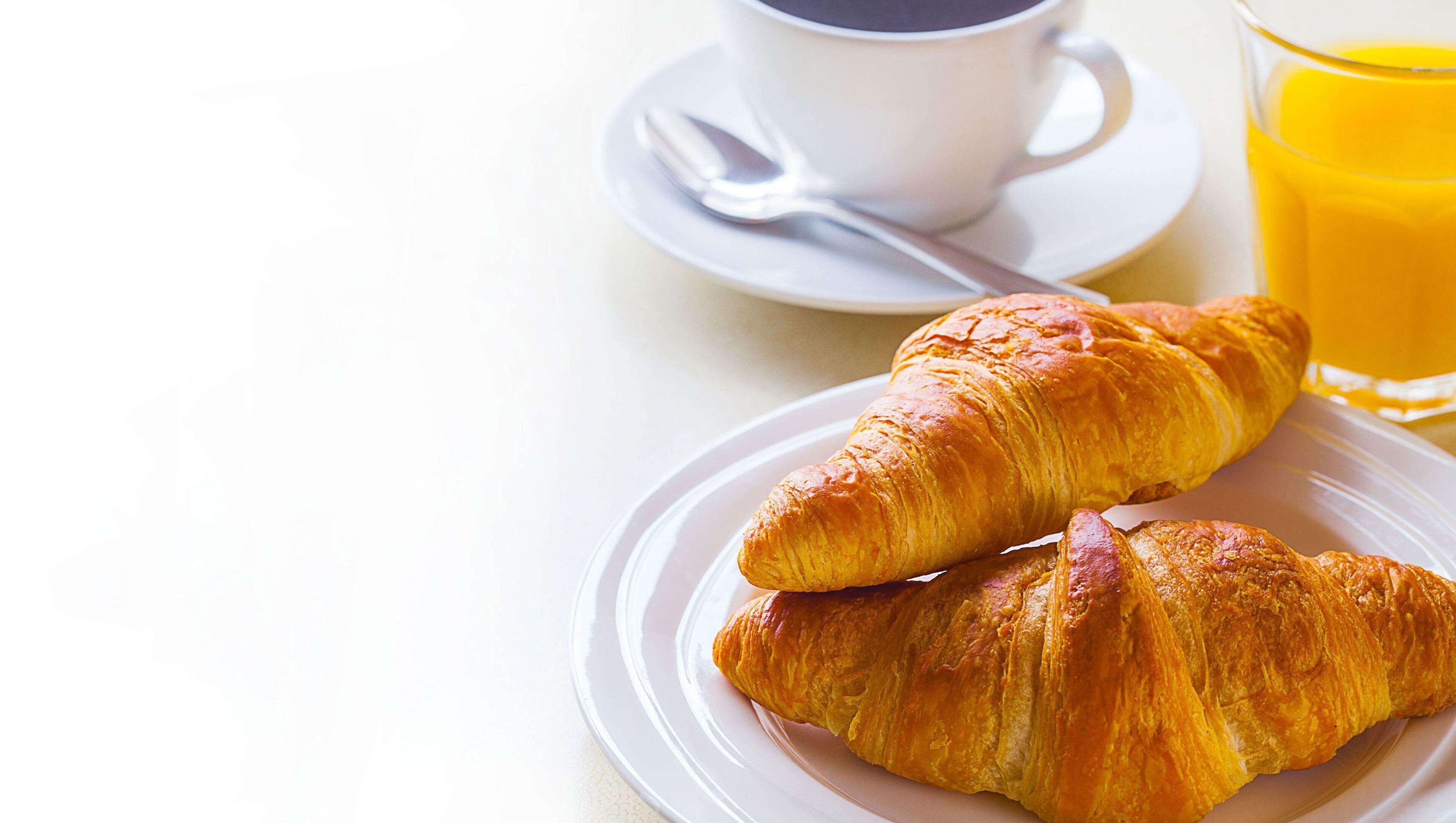Two croissants on a plate, a cup of coffee, and a glass of orange juice.