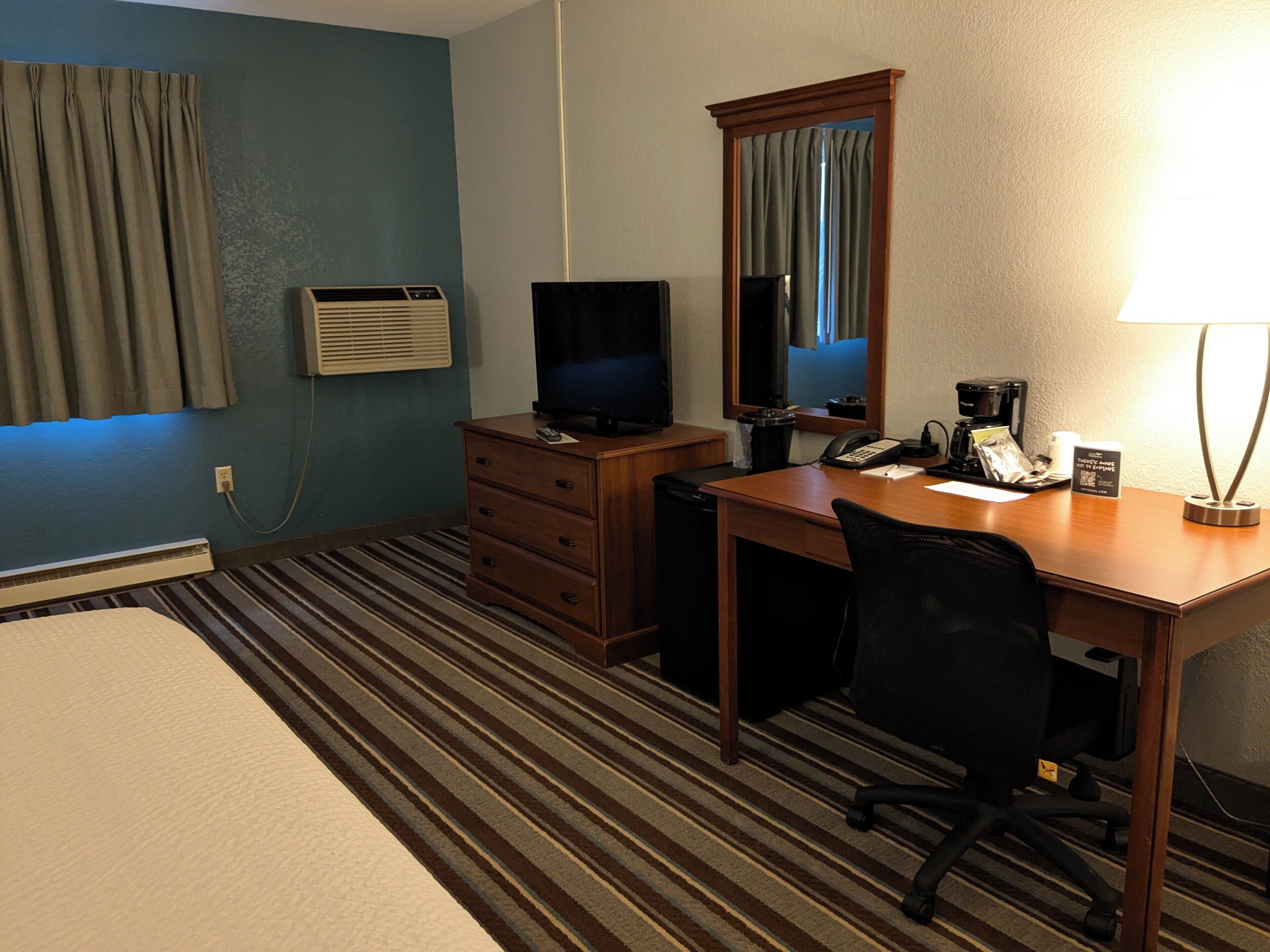 A hotel room with a bed, a desk with a chair, a television, a telephone, and a lamp.