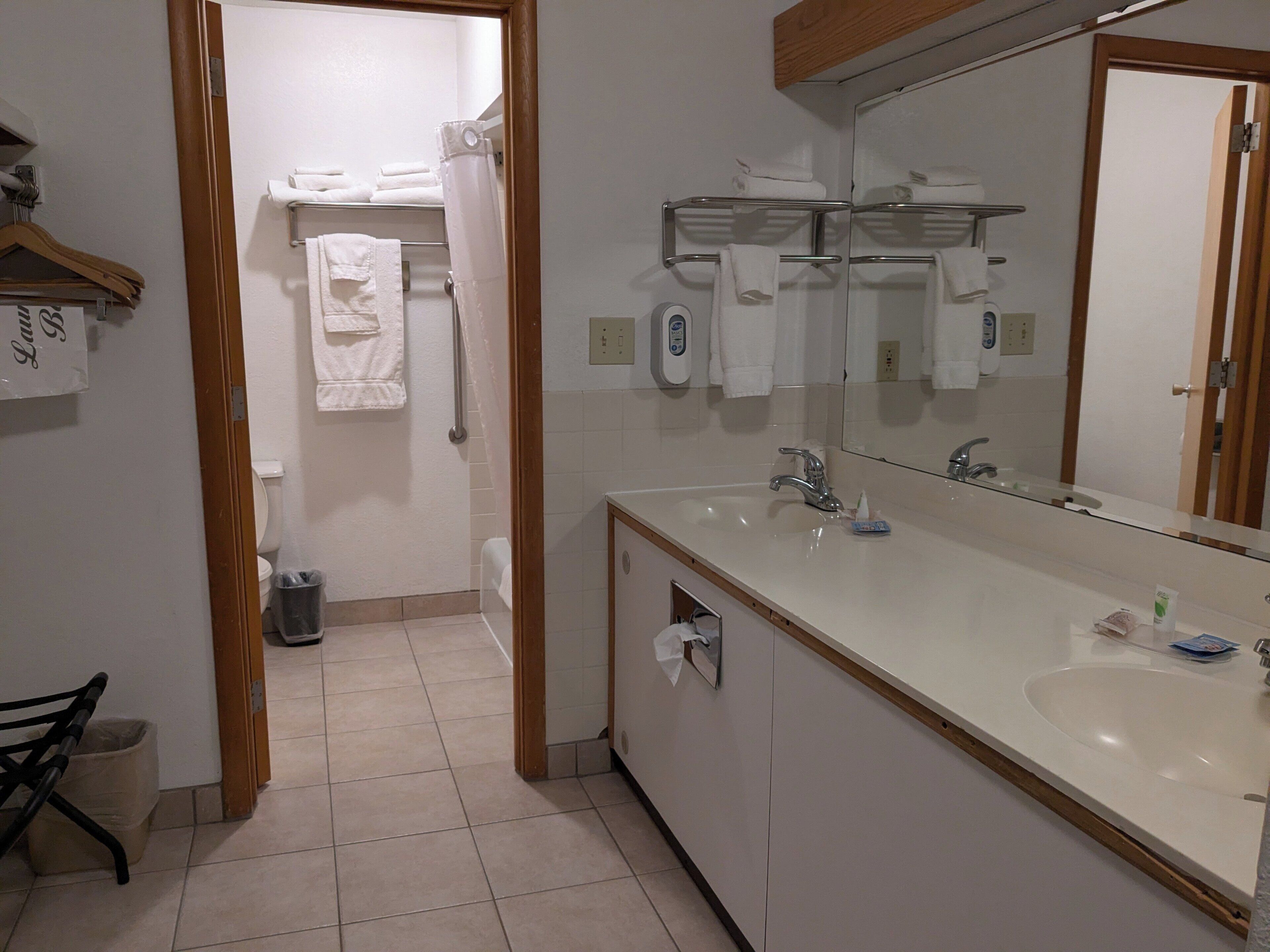 A modern bathroom with a large mirror, a sink, and a toilet. There are towels and a hand dryer on the wall.