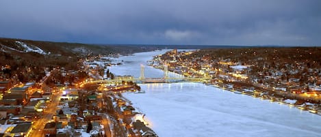 A snow-covered town with a river, a bridge, and illuminated buildings.
