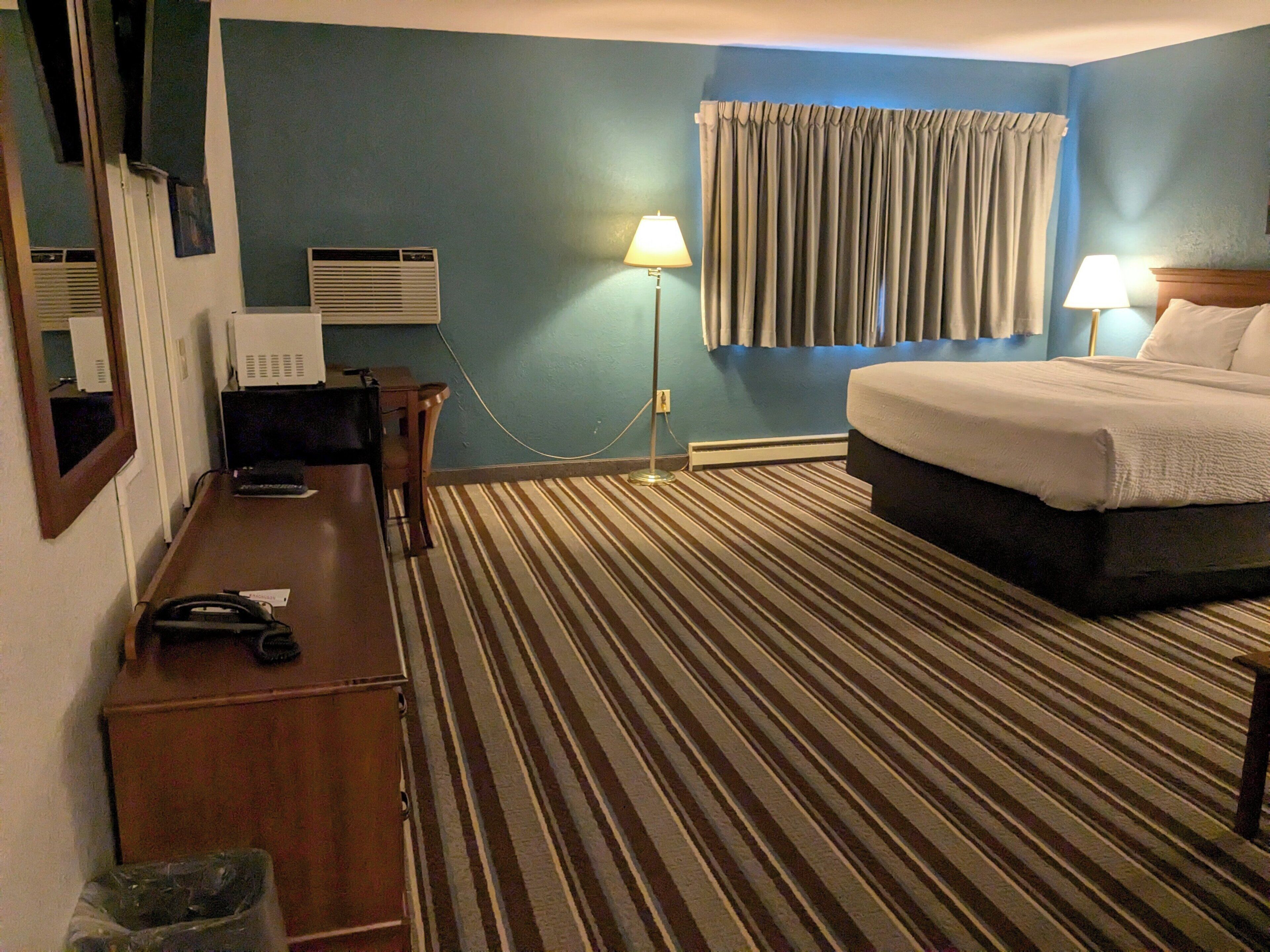 A hotel room with a bed, desk, and lamps.