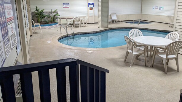 An indoor swimming pool area with a pool table, lounge chairs, and a staircase leading to an upper level. - Magnuson Hotel Copper Crown (Hancock)