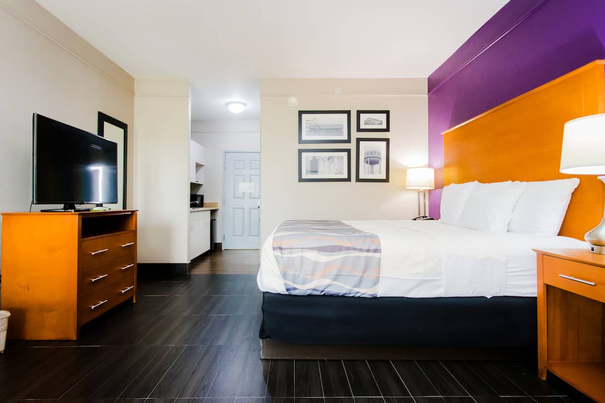 Habitación de hotel con cama, mesita de noche, lámpara, televisor, armario y baño visible a través de una puerta abierta.