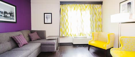 A living room with a grey sofa, two yellow armchairs, a purple wall, and a window with yellow curtains.