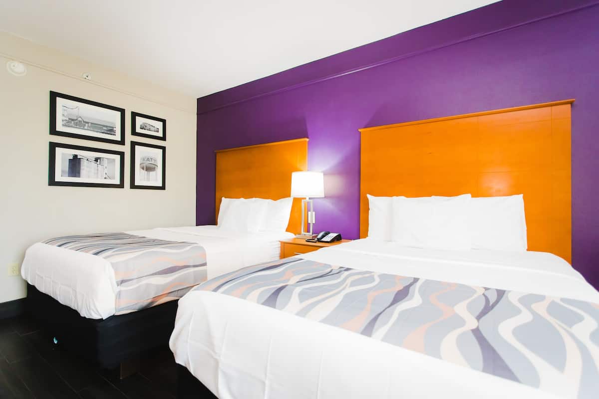 Una habitación de hotel con dos camas, una mesita de noche con lámpara y cuadros en la pared.