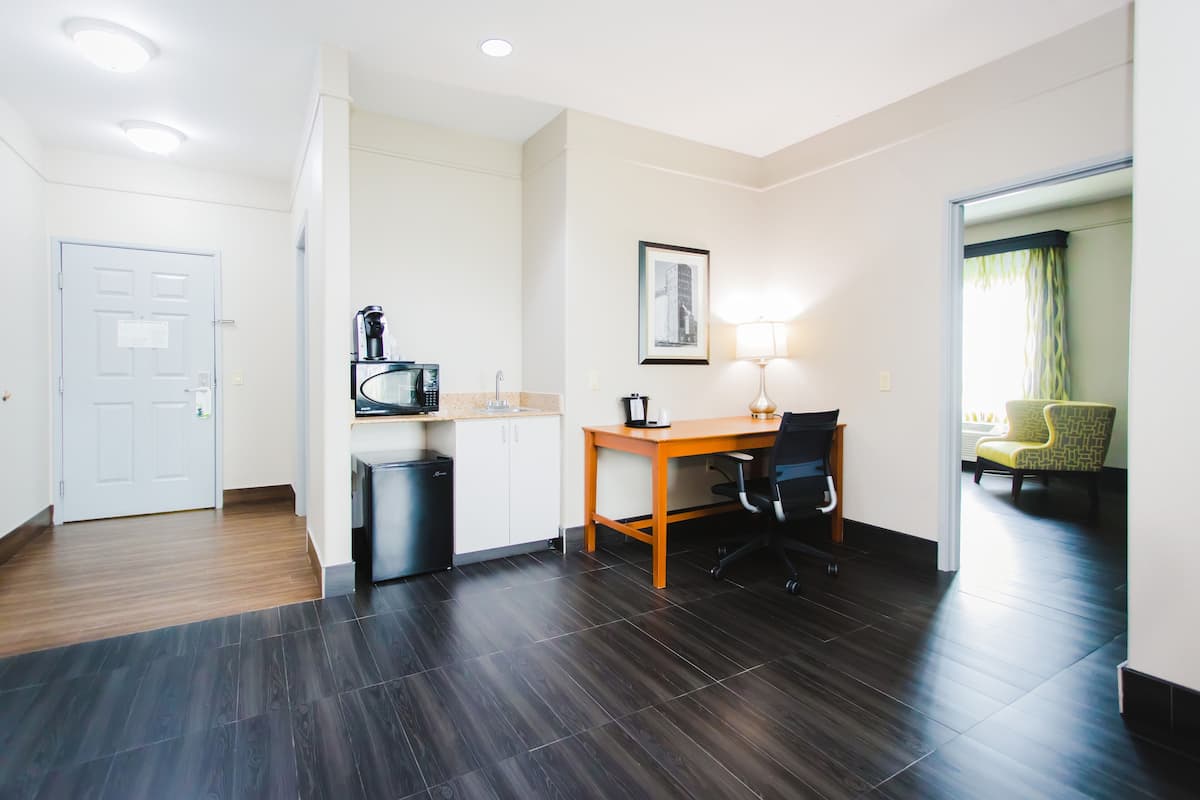 Habitación de hotel con un escritorio de madera, una silla, microondas, cubo de basura y un cuadro en la pared.