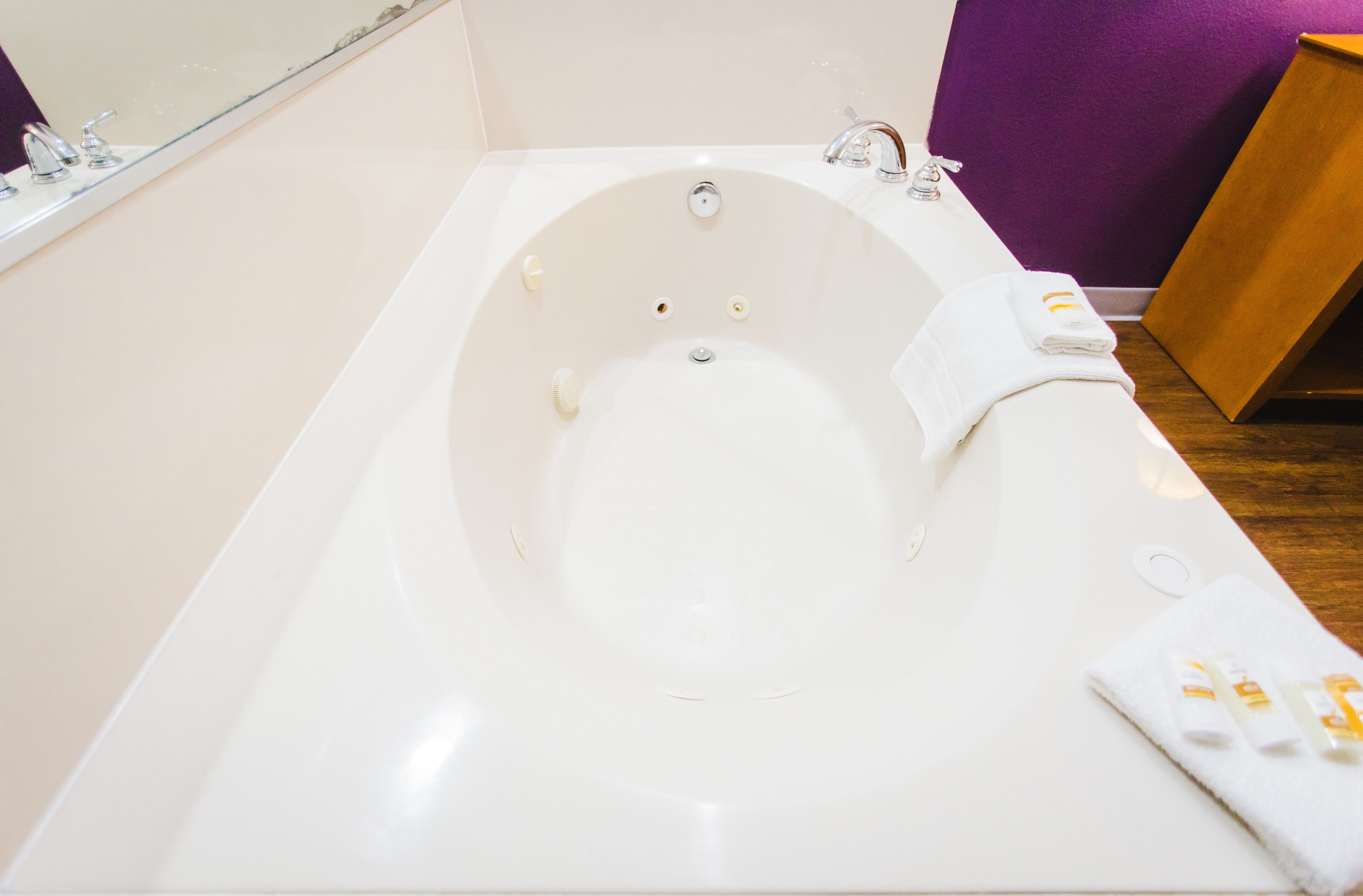 Une baignoire blanche avec un seul robinet, un petit miroir au-dessus et une table d’appoint en bois sur laquelle est posée une serviette.