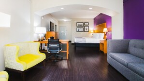 Quarto de hotel com cama, escrivaninha com cadeira, sofá e pequena mesa com abajur.