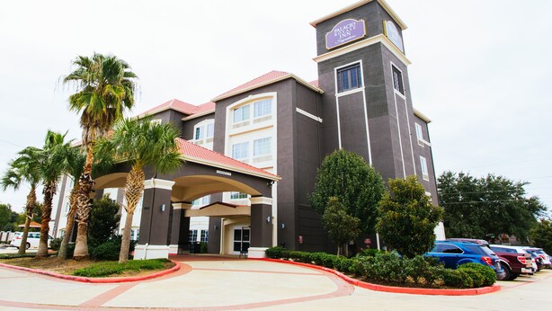 Um hotel com uma torre imponente, entrada coberta e estacionamento com vários carros.