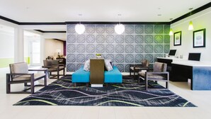 Um lobby de hotel moderno com uma mesa de recepção, dois sofás e uma parede estampada.