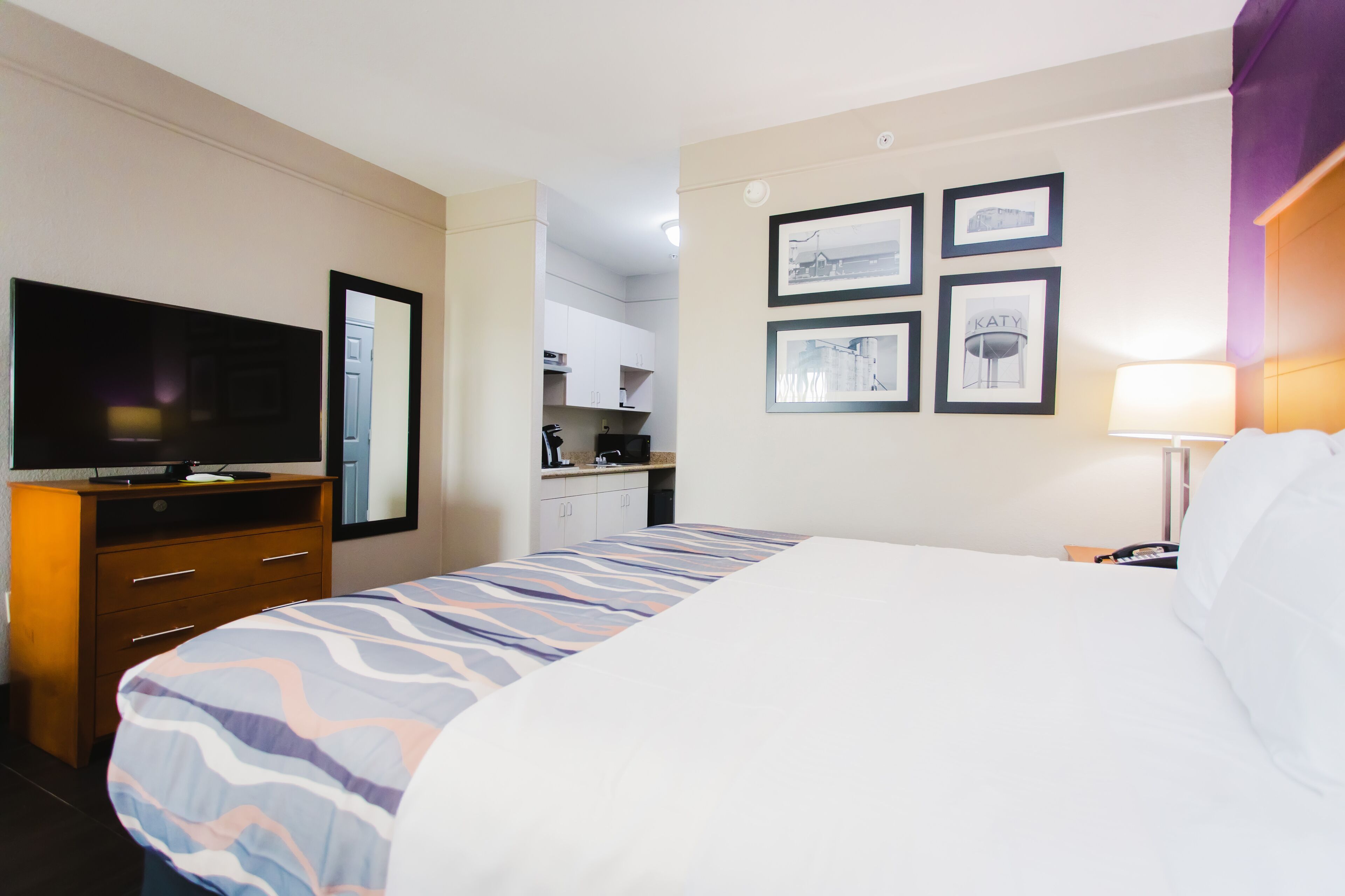 Ein Hotelzimmer mit Bett, Fernseher, Schreibtisch und einer Küchenzeile.