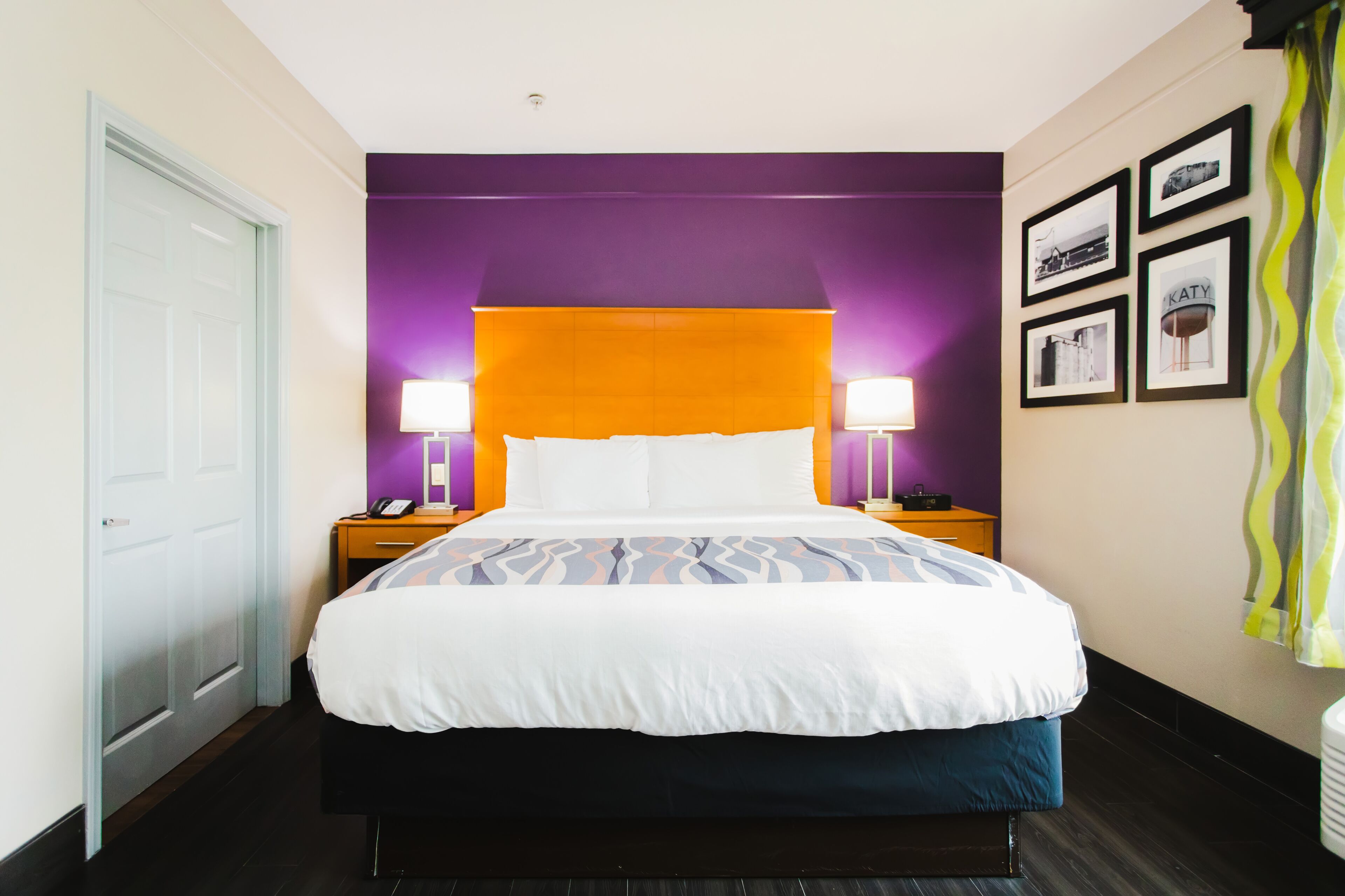 A hotel room with a bed, two bedside tables, a nightstand, a door, and a wall with framed pictures.