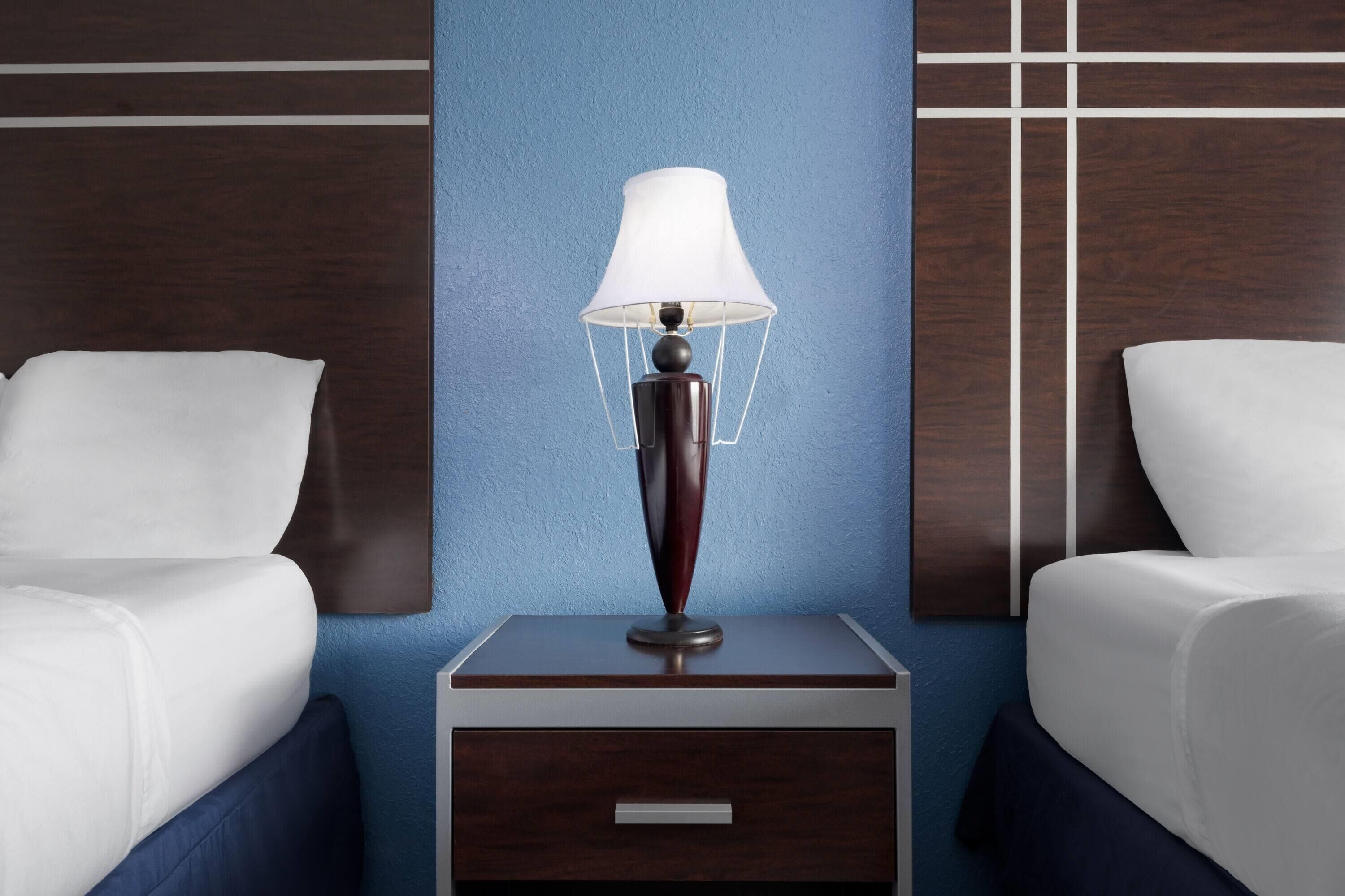 A hotel room with two beds, a bedside table with a lamp, and a wall with a geometric pattern.