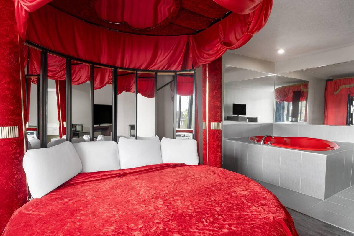Une chambre à coucher moderne avec un grand lit, un baldaquin rouge, un grand miroir et une baignoire rouge.