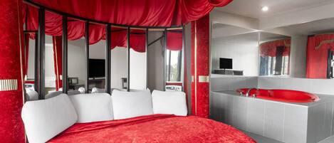 A modern bedroom with a large bed, a red canopy, a large mirror, and a red bathtub.