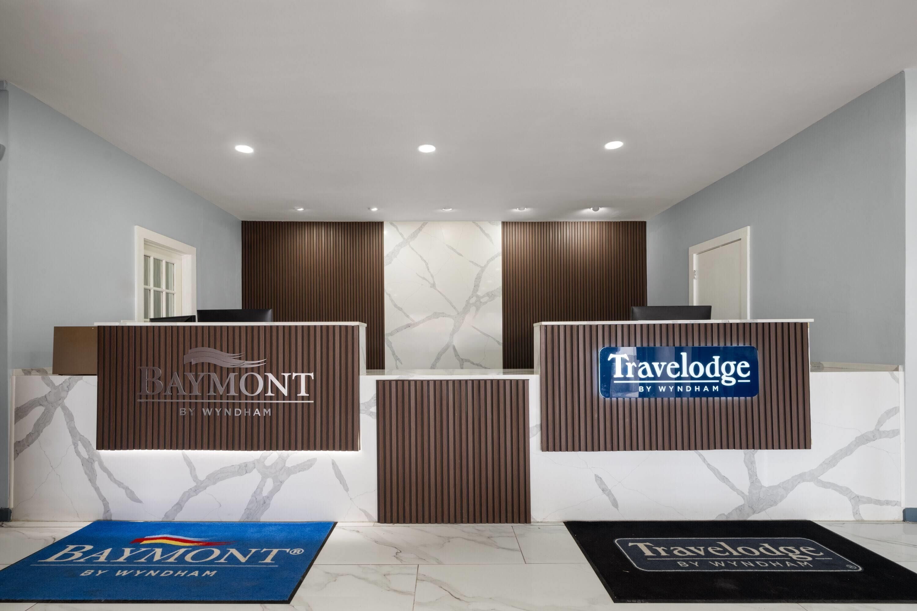 Un área de recepción con dos mostradores identificados como 'Baymont by Wyndham' y 'Travelodge by Wyndham'.