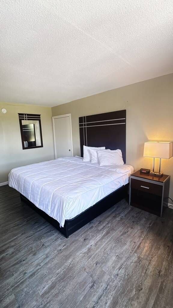 A hotel room with a large bed, a nightstand with a lamp, and a door.