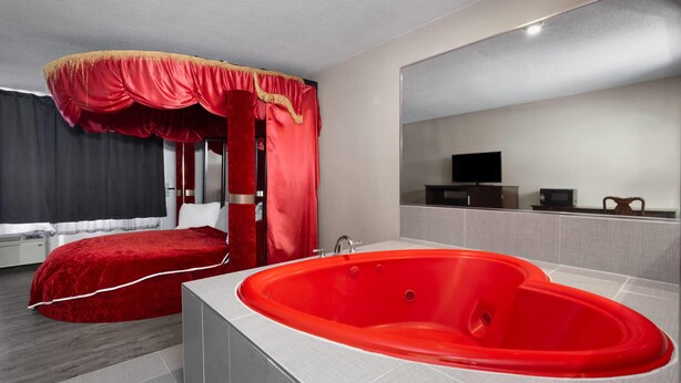 Ein modernes Hotelzimmer mit einem roten Himmelbett, einer großen, roten Badewanne und einem Fernseher an der Wand.